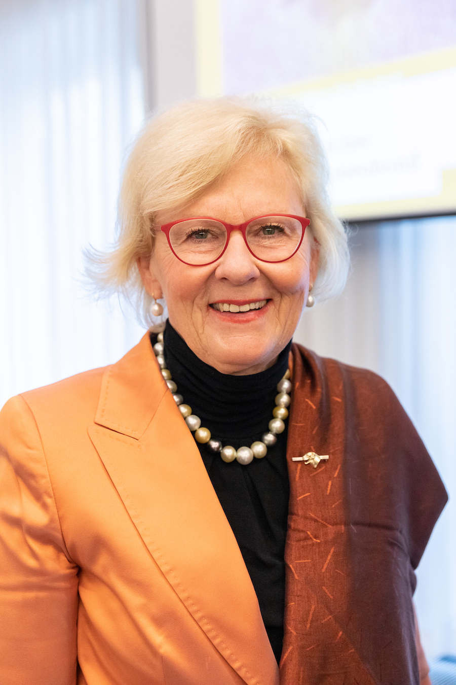 Person im orangen Blazer mit Perlenkette und braunem Schal, buhren