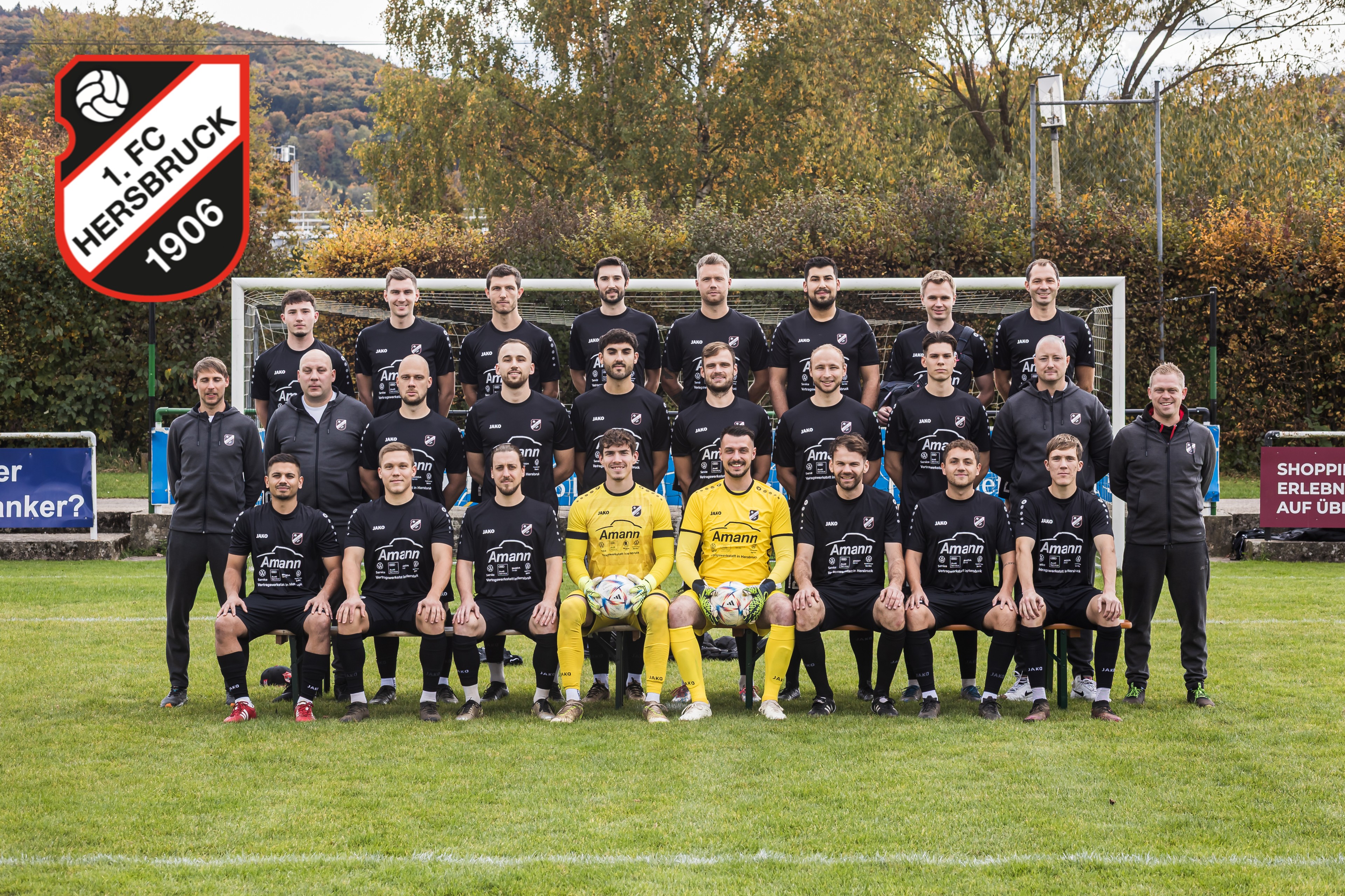 Mannschaftsfoto eines Fußballteams in schwarzen Trikots mit Amann-Werbung, aufgenommen vor einem Tor auf einem Fußballplatz