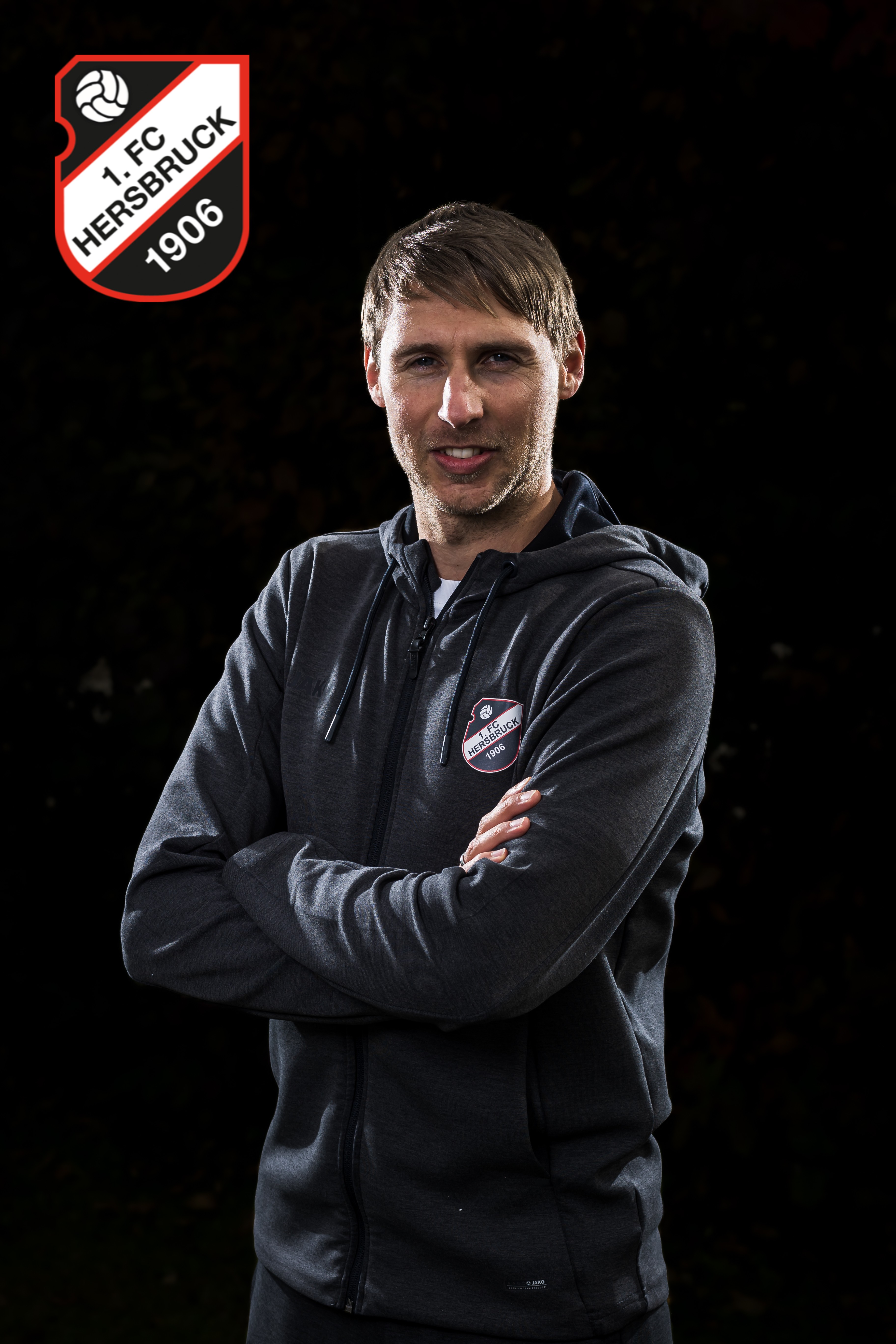 Person mit Hoodie des Vereins Herrenfußball 1906 vor schwarzem Hintergrund