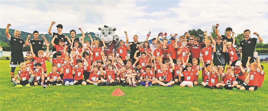 Gruppenfoto von Kindern im Jugendfußballcamp mit Maskottchen und Trainer.