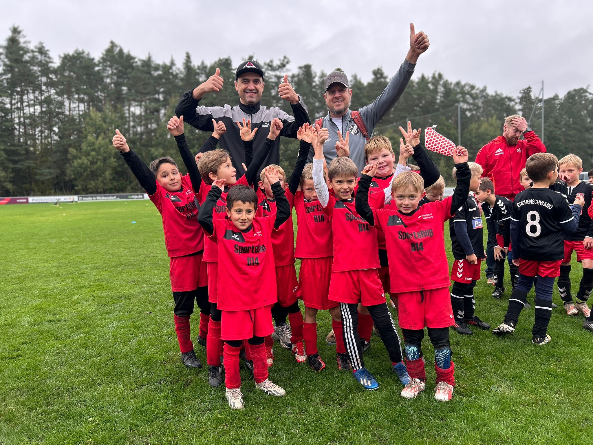 Kinderfußballmannschaft in roten Trikots jubelt auf dem Sportplatz