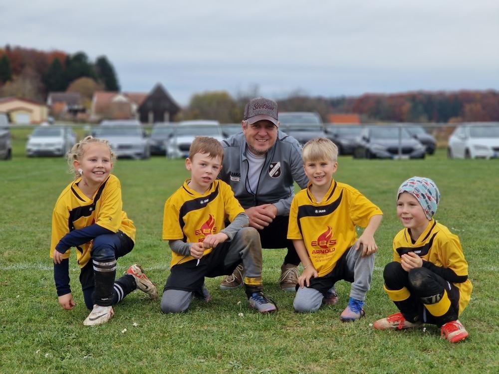 Kinderfußballmannschaft mit Trainer auf dem Sportplatz, gelbe Trikots mit EBS Arnold Logo