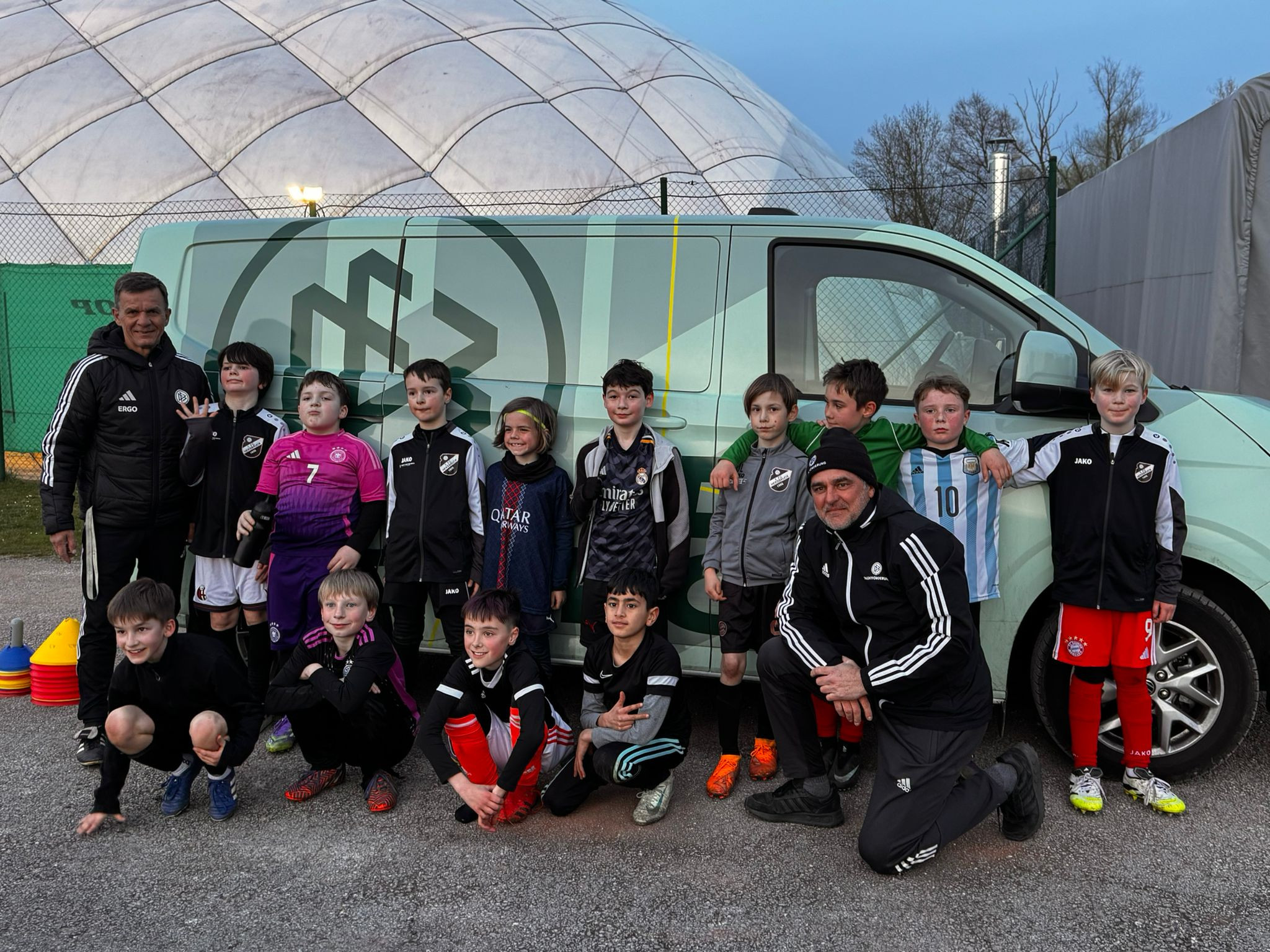 Kinderfußballmannschaft und Trainer vor Vereinsbus, Gruppenfoto am Sportplatz, aufgenommen am Abend