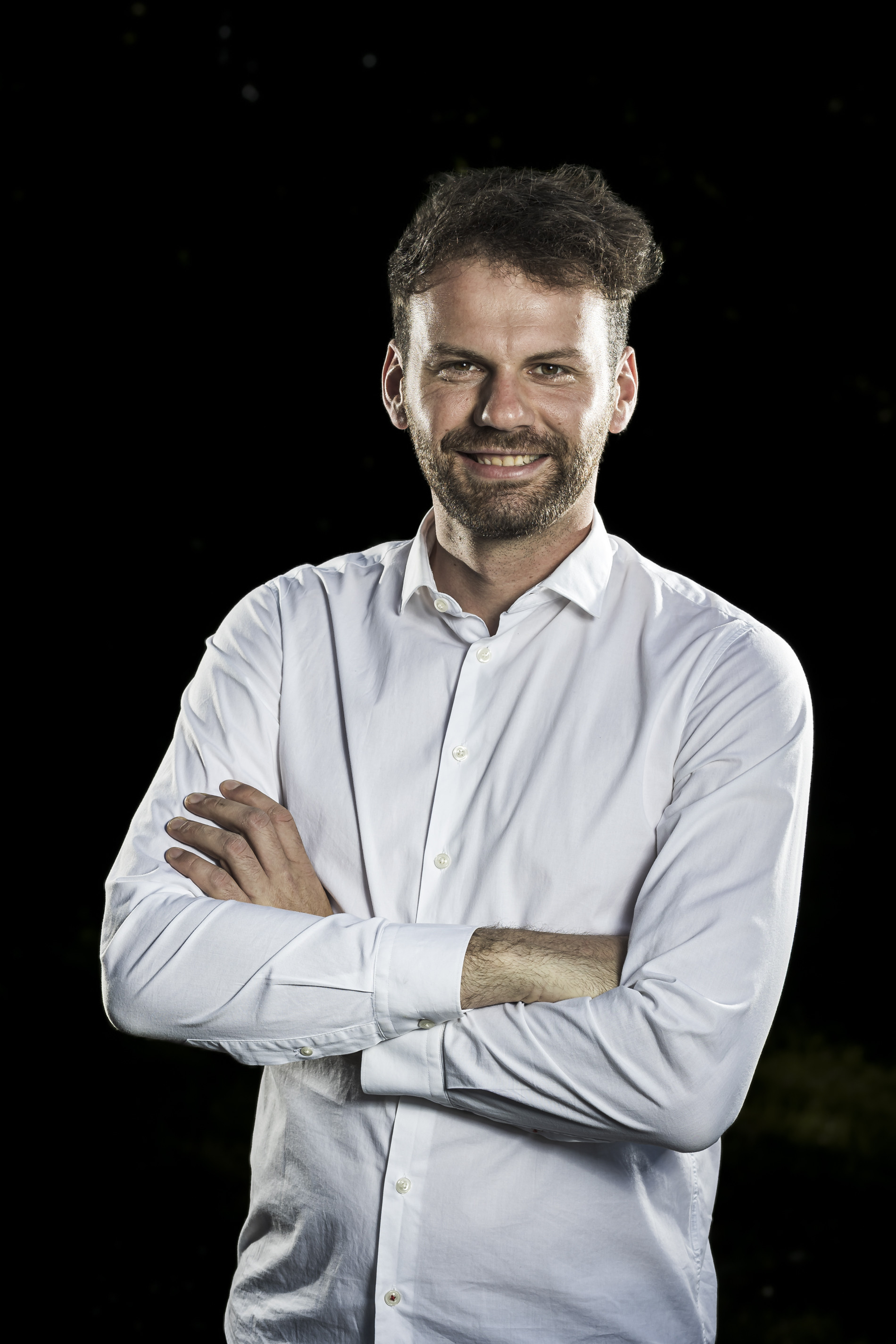 Porträt eines lächelnden Mannes mit weißem Hemd vor schwarzem Hintergrund