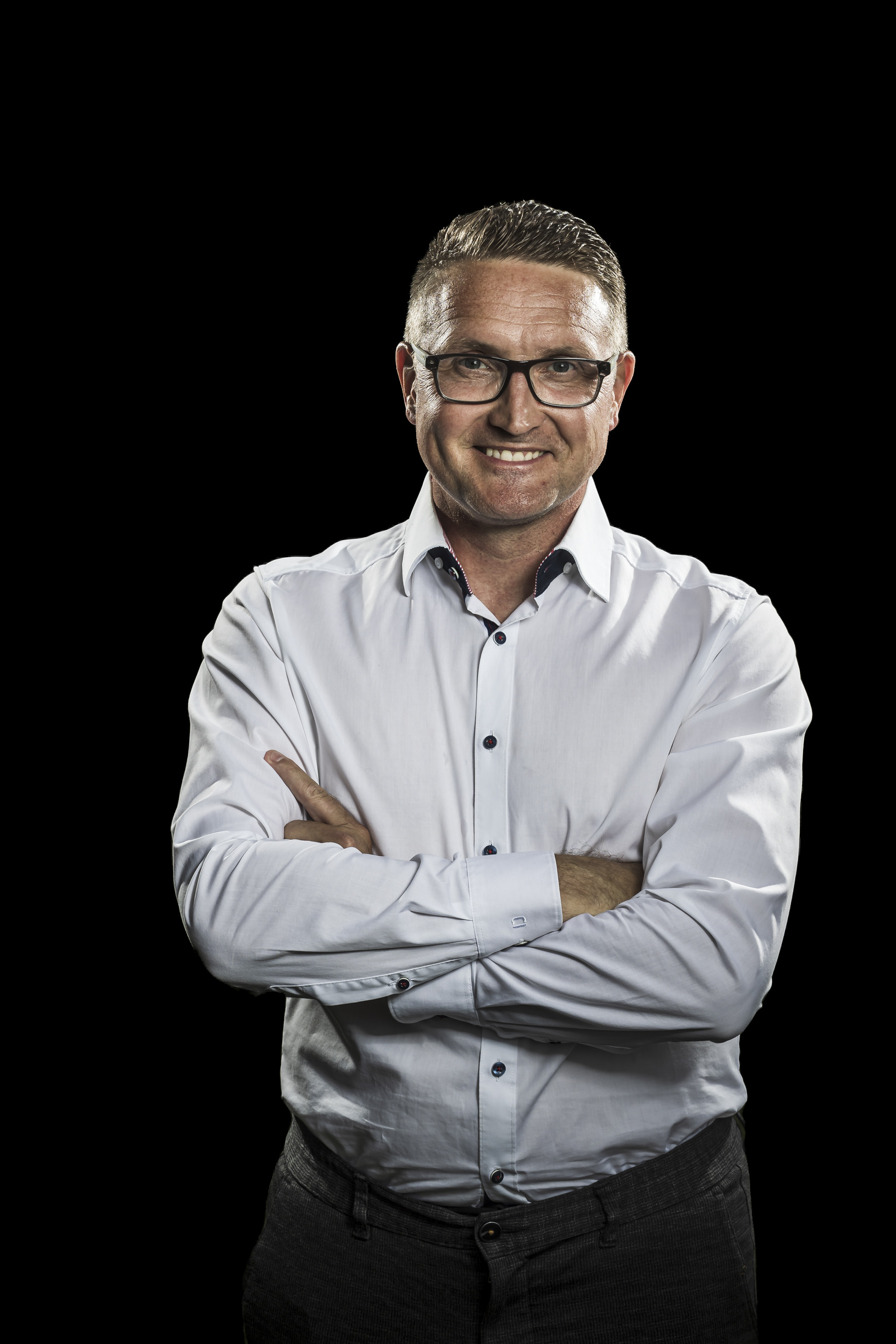 Business-Porträt eines Mannes mit verschränkten Armen in weißem Hemd vor schwarzem Hintergrund, y22a1696