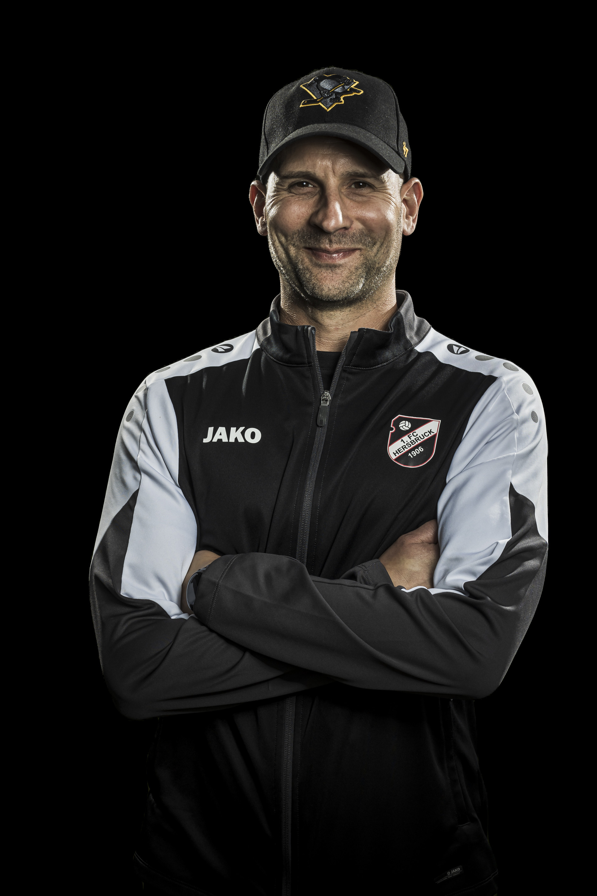 Trainer des FC Heßelsbruck 1906 in JAKO Trainingsjacke mit verschränkten Armen vor schwarzem Hintergrund