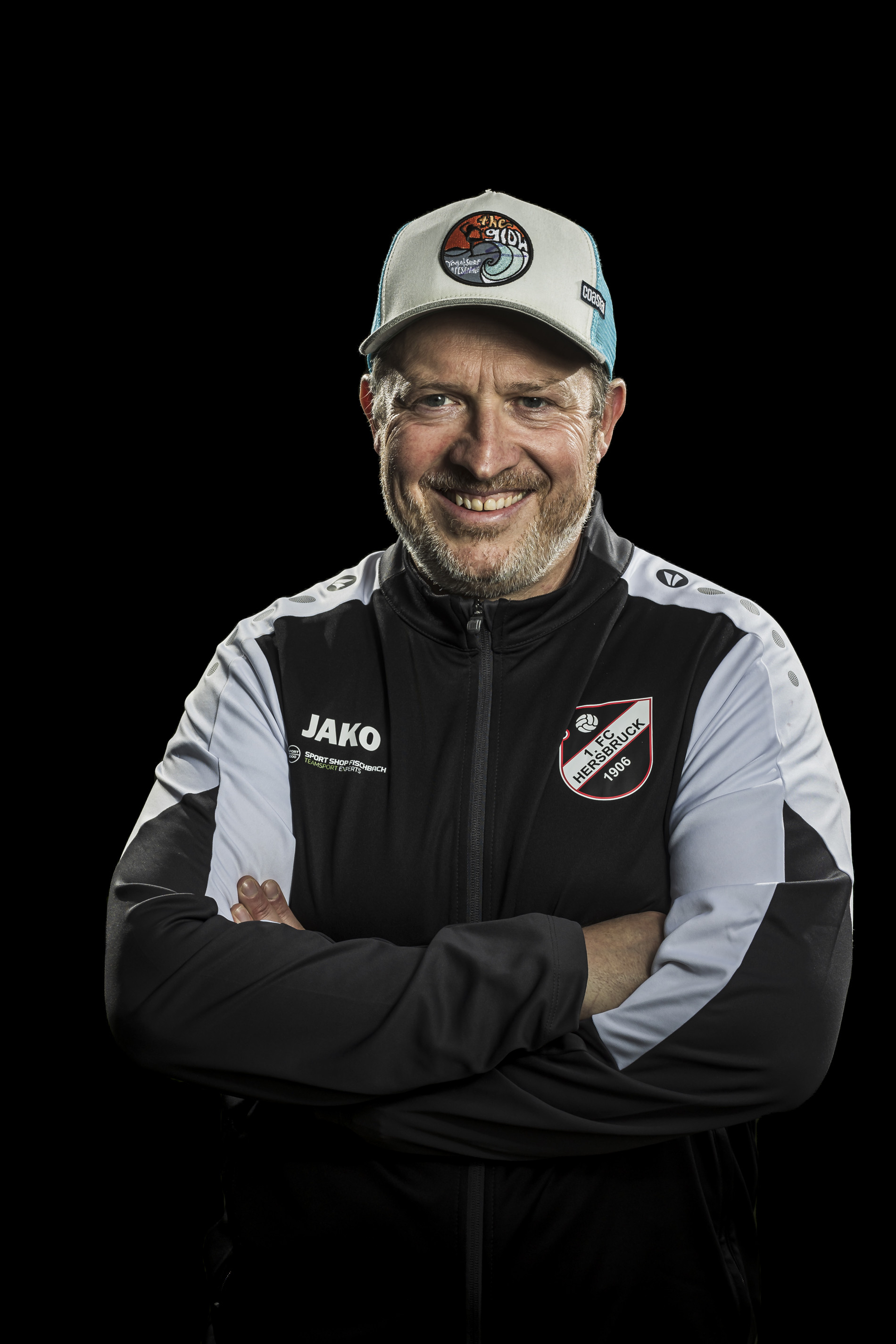 Trainer des 1. FC Hersbruck mit Vereinsjacke und Cap, Portraitfoto vor schwarzem Hintergrund