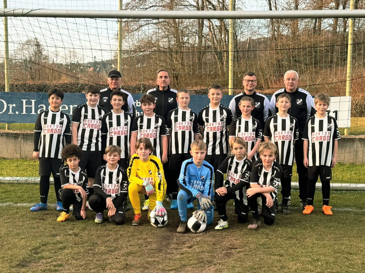 Jugend-Fußballmannschaft mit Trainern im Gruppenfoto auf dem Sportplatz, schwarz-weiße Trikots, Sponsoring durch Doktor Cargo