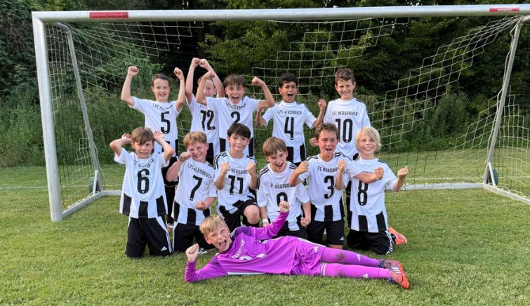 Jubelnde Kinderfußballmannschaft des FC Heesbacher vor einem Tor, Spieler in weißen Trikots, darunter Max