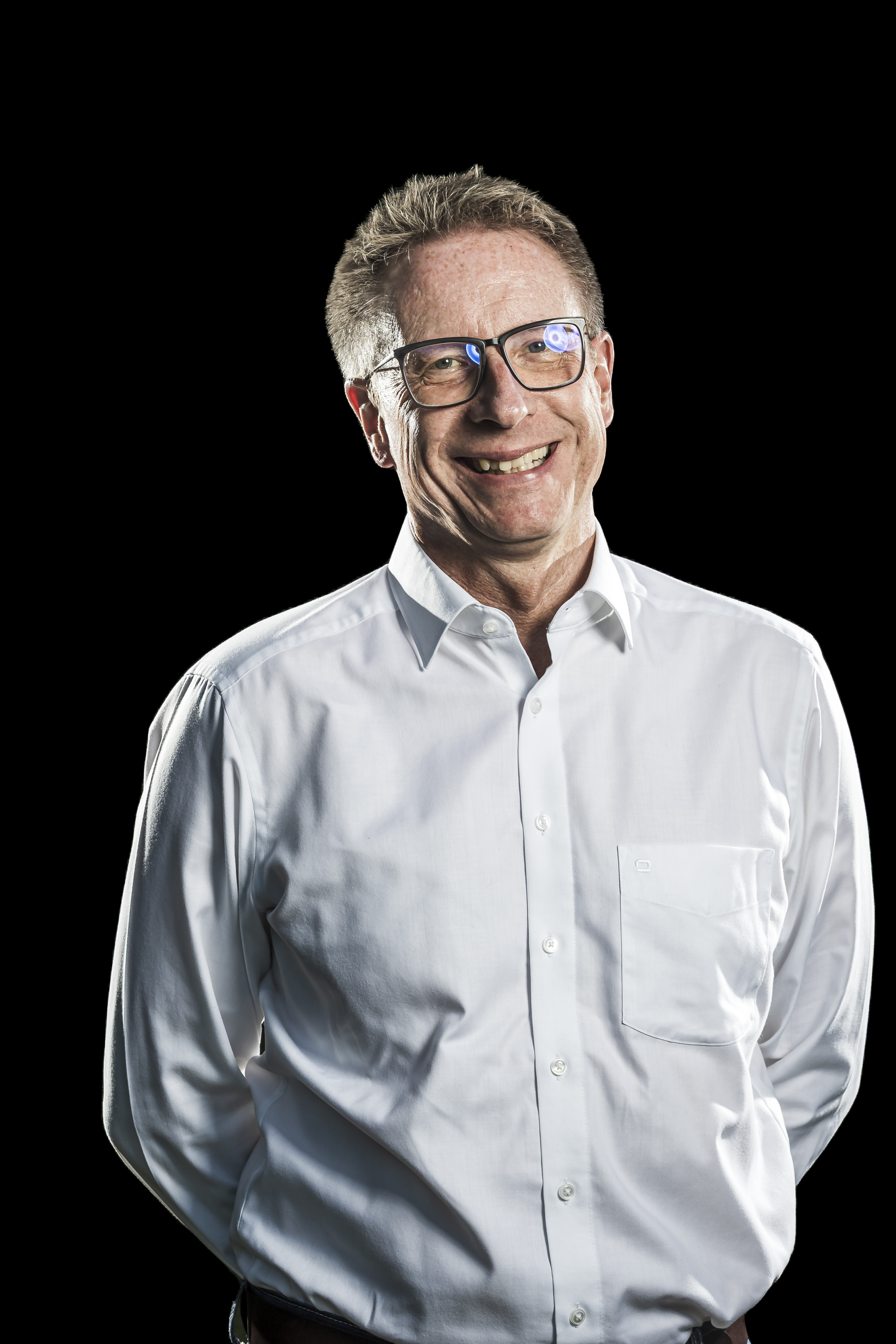 Porträt eines lächelnden Mannes mit Brille und weißem Hemd vor schwarzem Hintergrund