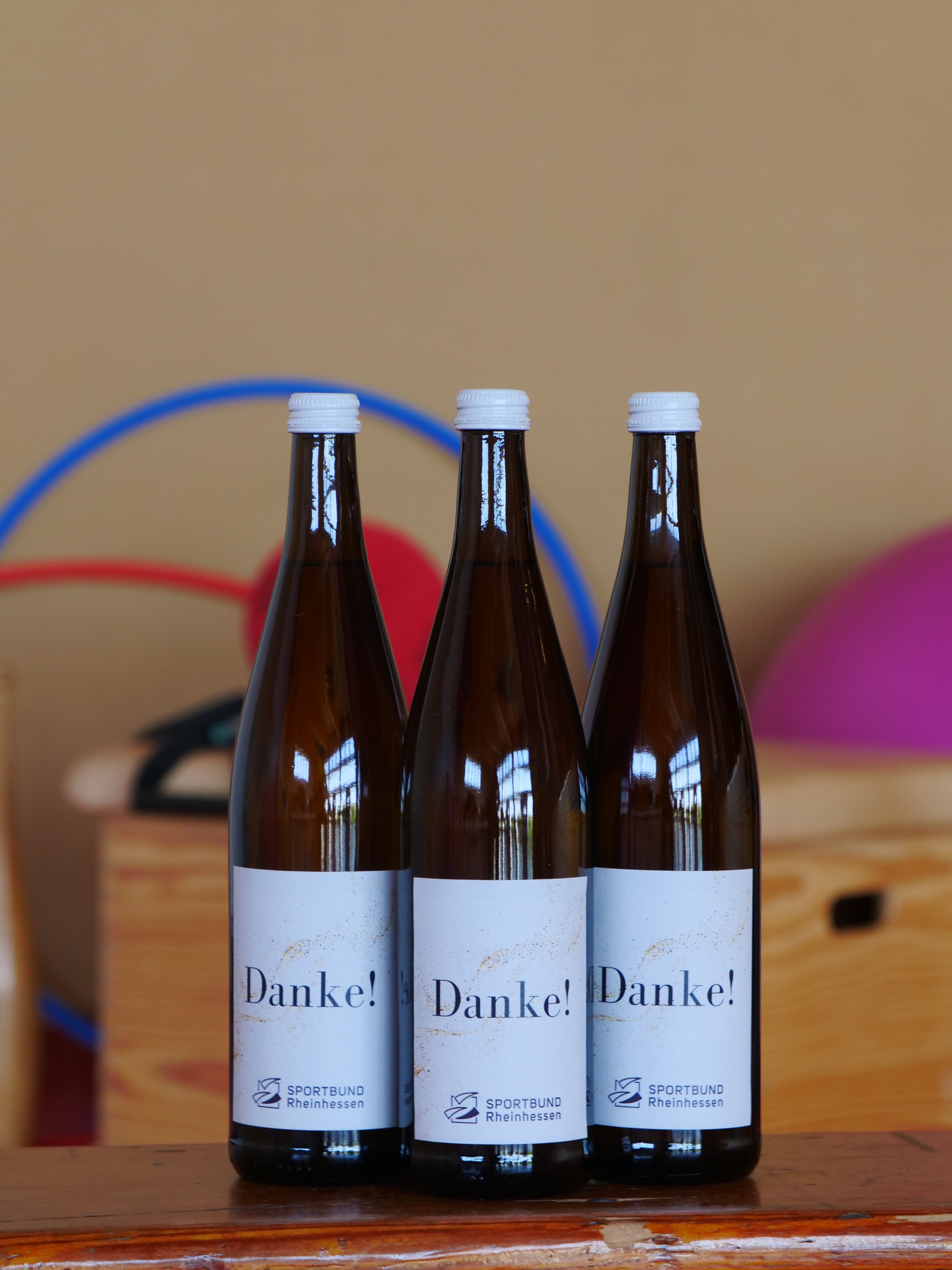 Drei Weinflaschen mit der Aufschrift Danke in einem Raum mit Sportgeräten
