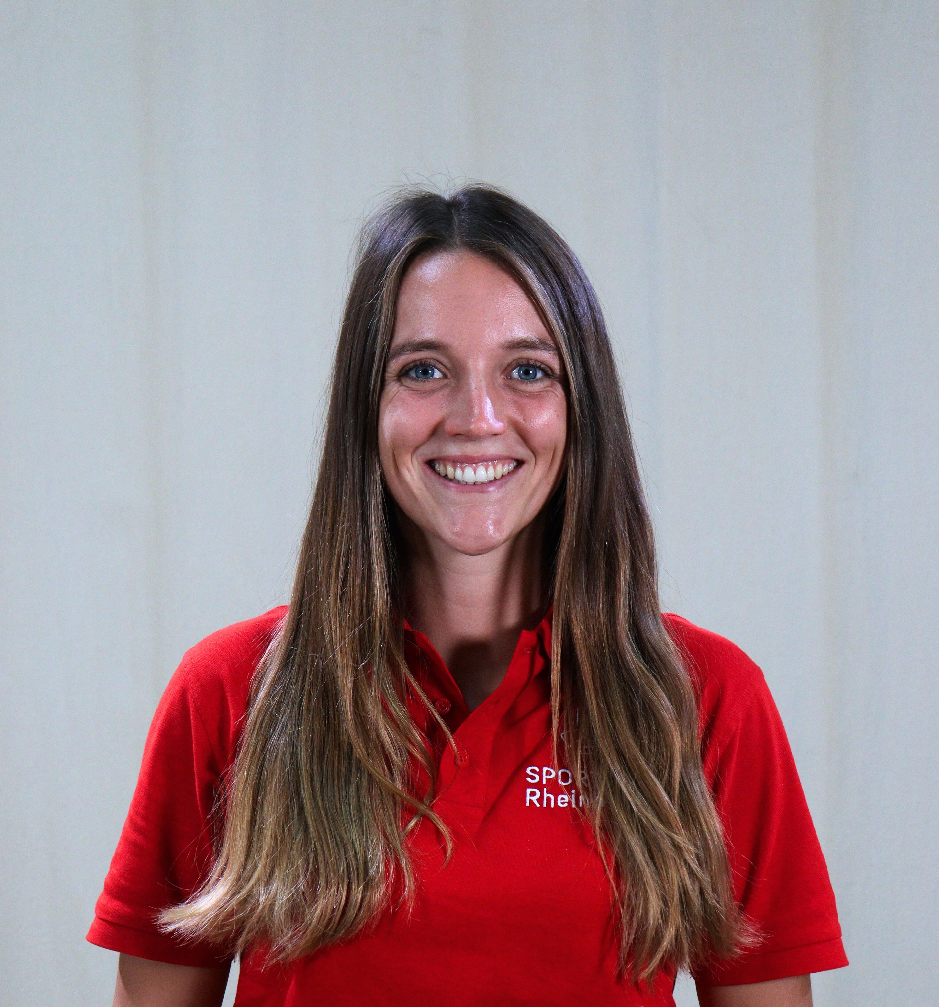 Frau mit langen braunen Haaren im roten Polohemd mit Aufschrift 'SPÖ Rhein' vor neutralem Hintergrund