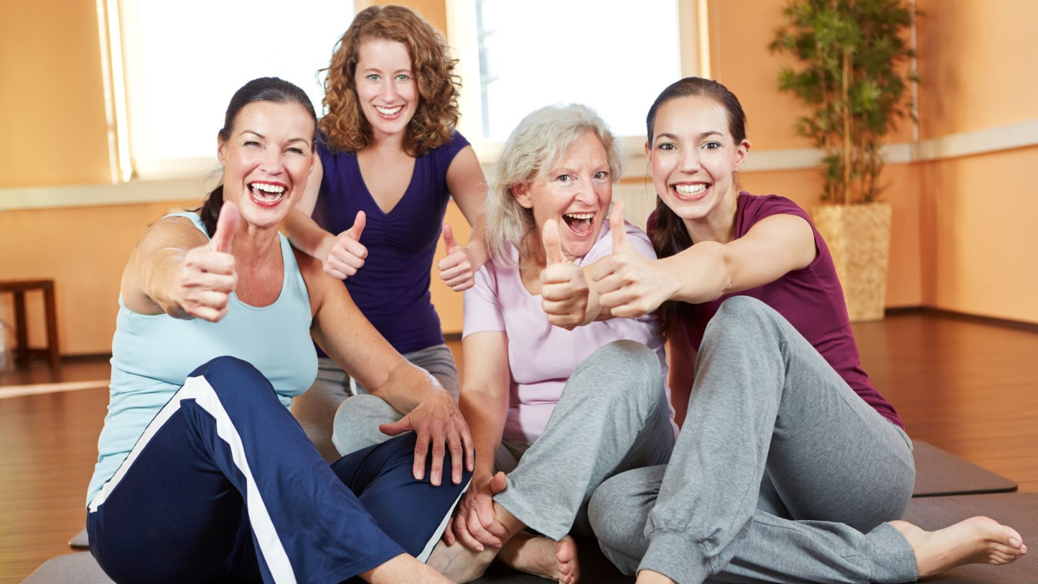 Gruppe von Frauen beim gemeinsamen Sport im Fitnessstudio mit Daumen hoch Geste