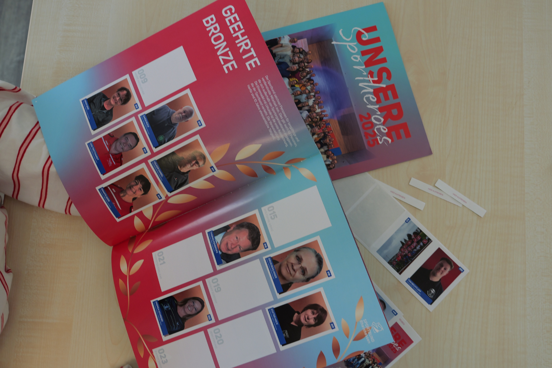 Offenes Stickeralbum 'Unsere Sportheroes 2025' mit Bildern geehrter Sportler in der Kategorie Bronze auf einem Tisch