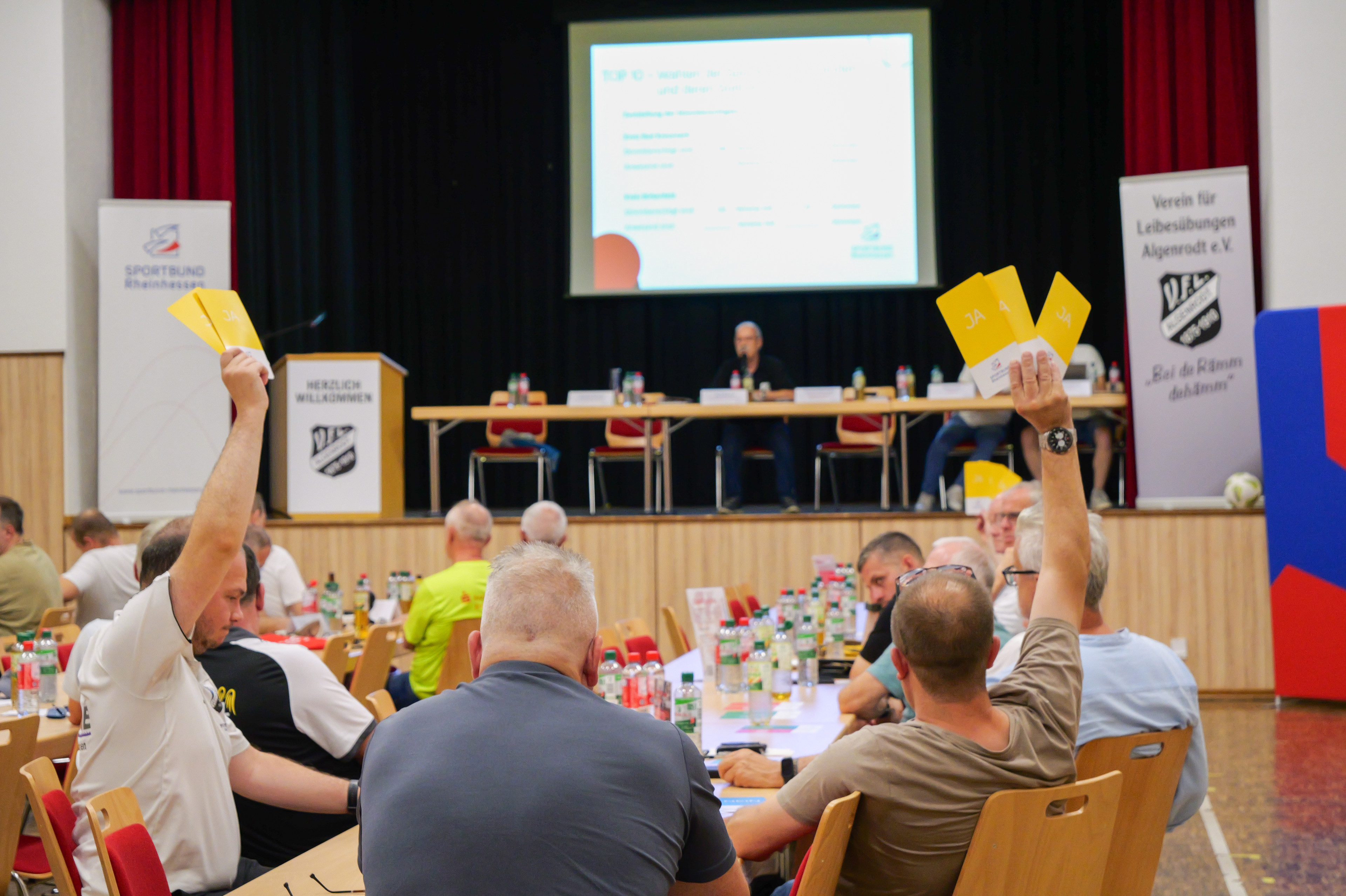 Mitglieder stimmen bei einer Versammlung mit gelben Karten ab, Podium im Hintergrund