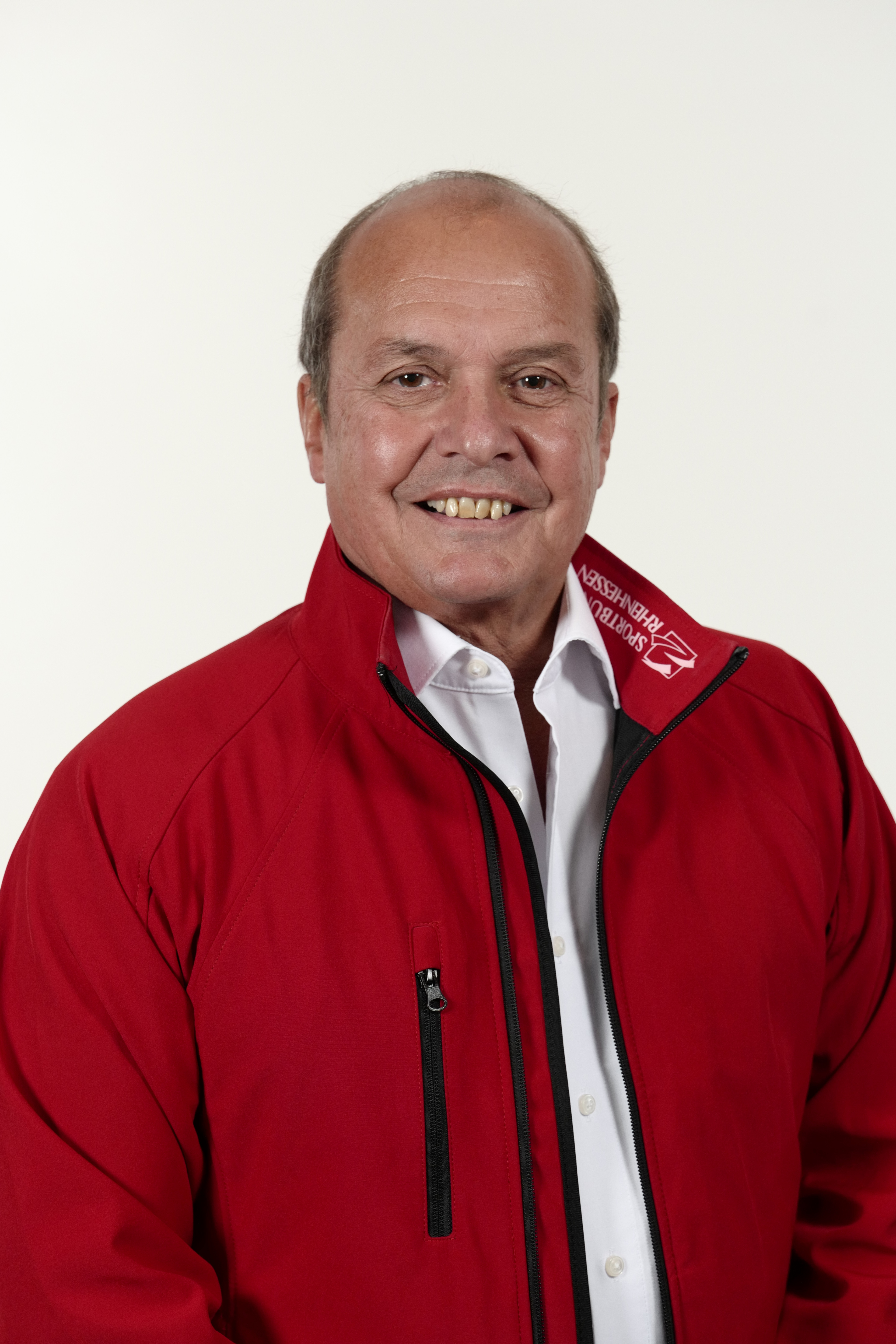 Porträt von Klaus Kuhn in roter Jacke vor weißem Hintergrund