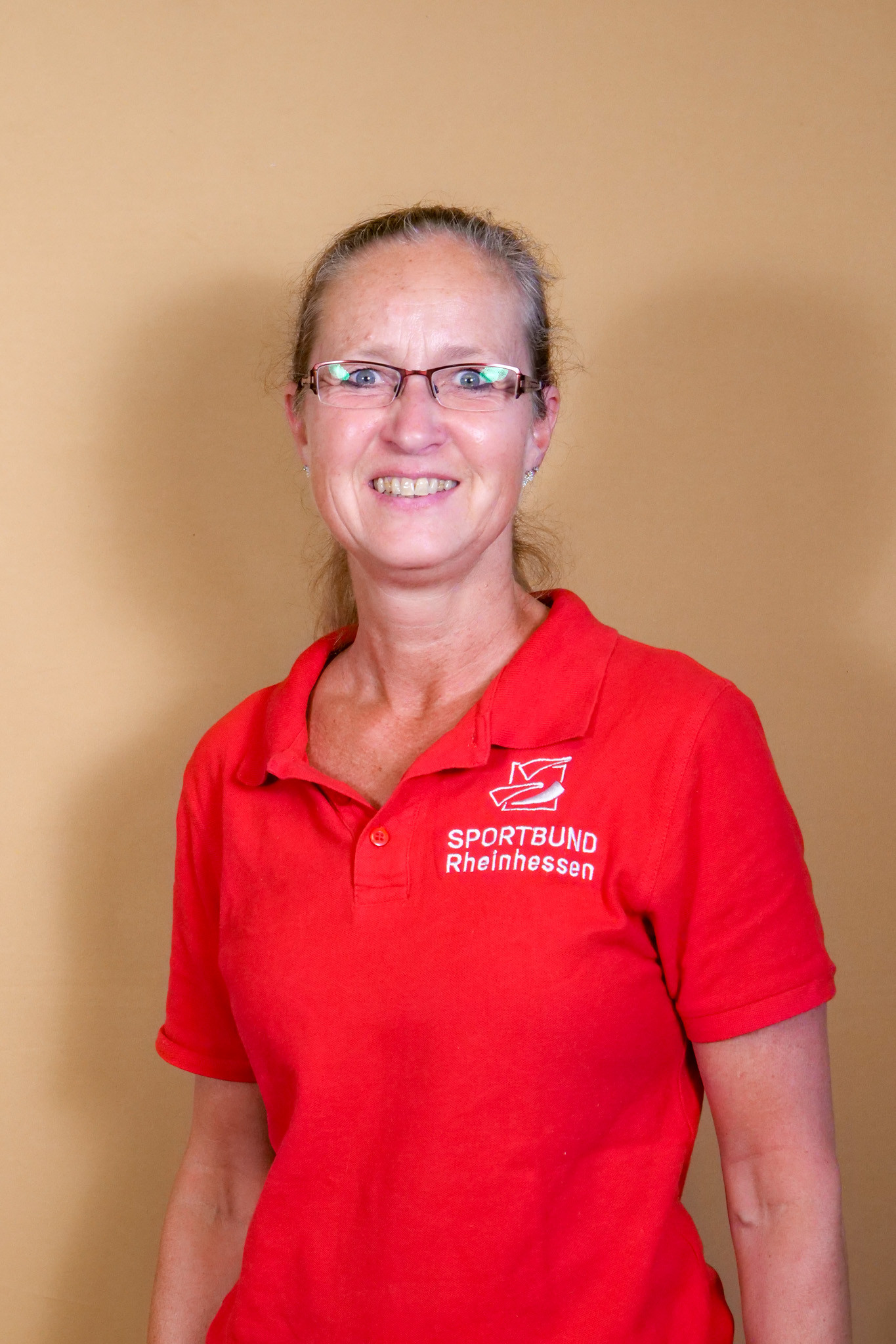 Frau mit Brille im roten Poloshirt des Sportbund Rheinhessen vor beigem Hintergrund