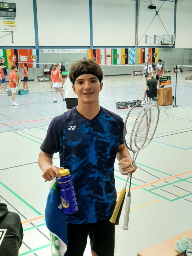 Aaron beim Badminton-Turnier in der Sporthalle mit Badmintonschlägern und Wasserflasche
