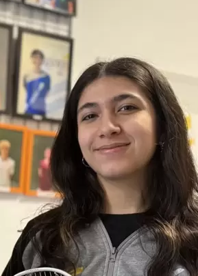 Porträt von Naghmeh mit langen dunklen Haaren vor einer Wand mit Fotos