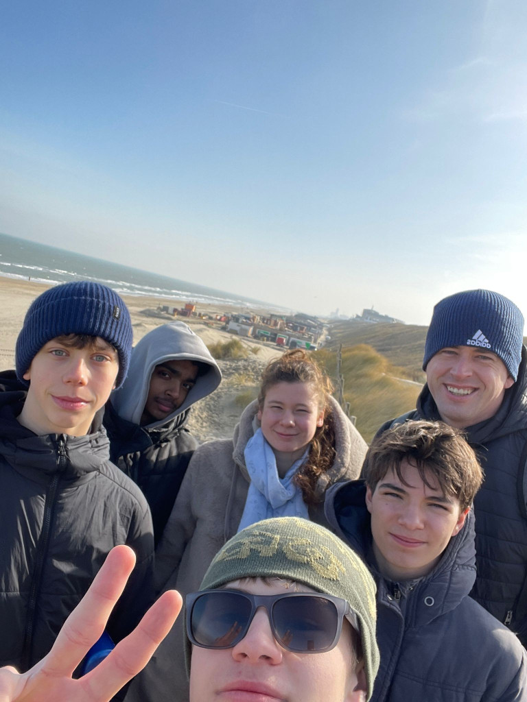 Gruppe von Menschen am Strand bei sonnigem Wetter, Dünen und Meer im Hintergrund
