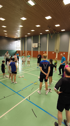 Kinder und Jugendliche beim Badminton-Training in einer Sporthalle, Trainer gibt Anweisungen, Gruppenaktivität