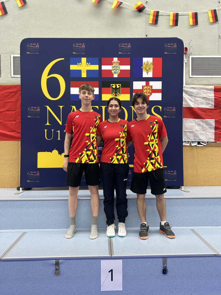 Drei deutsche Badmintonspieler bei den 6 Nations U15 vor einer Länderflaggen-Wand