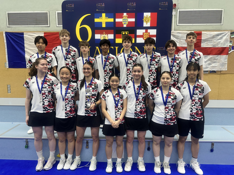Gruppenfoto einer Badminton-Mannschaft bei den 6 Nations, Spielerinnen und Spieler mit Medaillen vor internationaler Flaggenwand