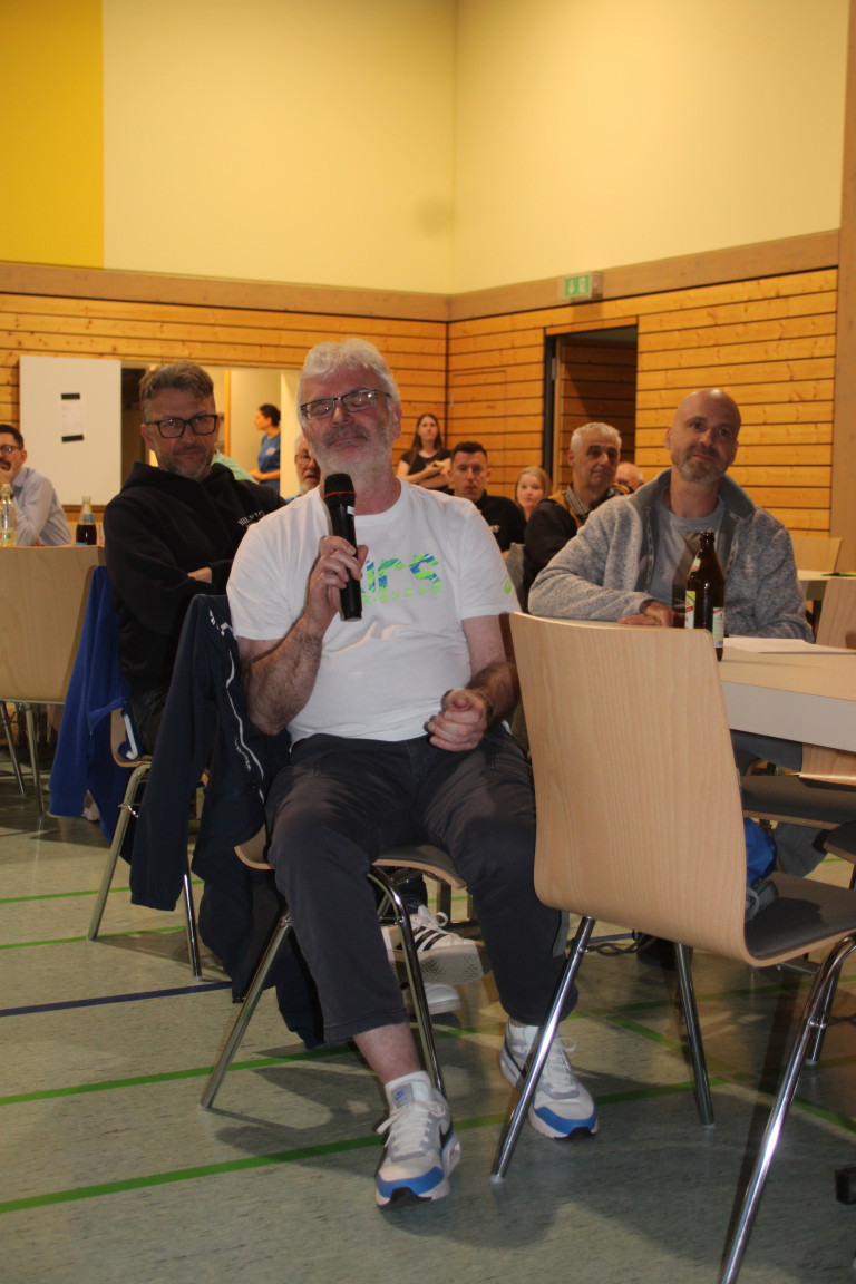 Mann spricht mit Mikrofon bei einer Veranstaltung in einem Gemeinschaftsraum