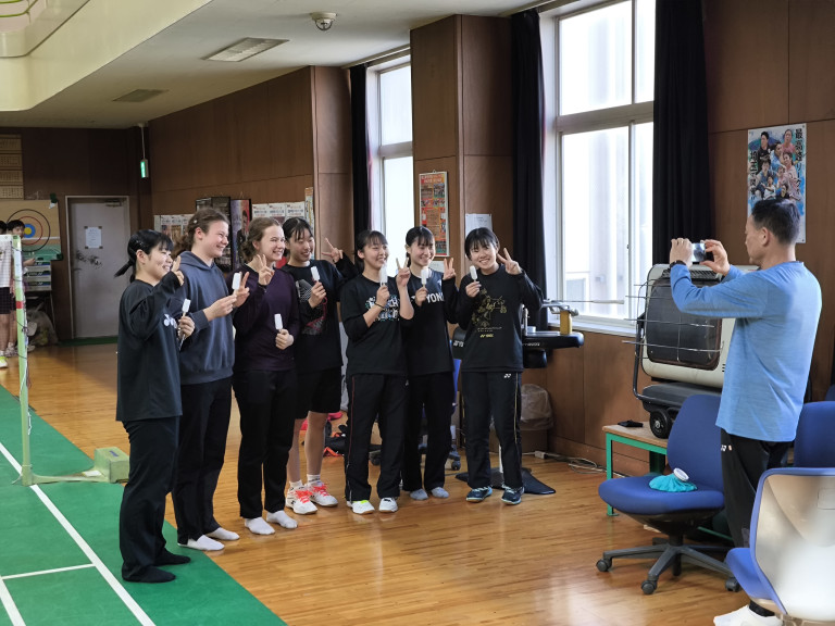 Gruppe von Jugendlichen posiert für ein Gruppenfoto in einem Sportraum, während eine Person das Foto macht.