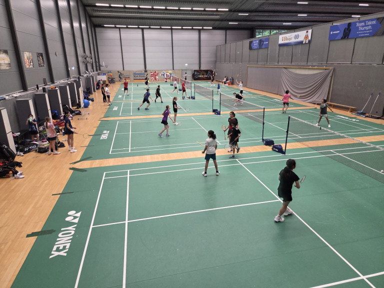 Kinder und Jugendliche spielen Badminton in einer modernen Sporthalle auf mehreren Feldern
