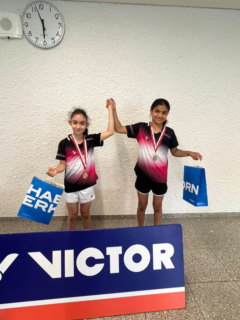 Zwei junge Badmintonspielerinnen mit Medaillen und Siegespose bei einem Turnier, Sponsoring durch Victor