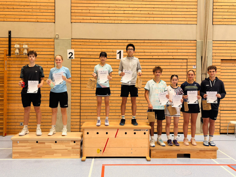 Jugendliche auf dem Siegerpodest bei einem Badminton-Turnier in einer Sporthalle, mit Urkunden und Preisen