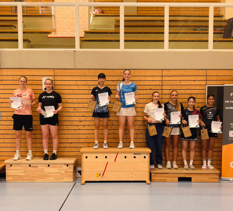 Siegerehrung bei einem Badminton-Turnier mit jungen Sportlerinnen in einer Sporthalle, die Urkunden und Preise halten.