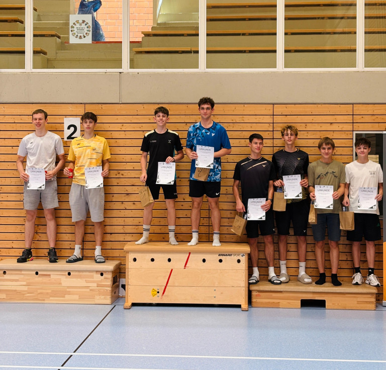 Siegerehrung bei einem Jugend-Sportturnier in einer Sporthalle, mehrere junge Männer stehen mit Urkunden und Preisen auf dem Podest.