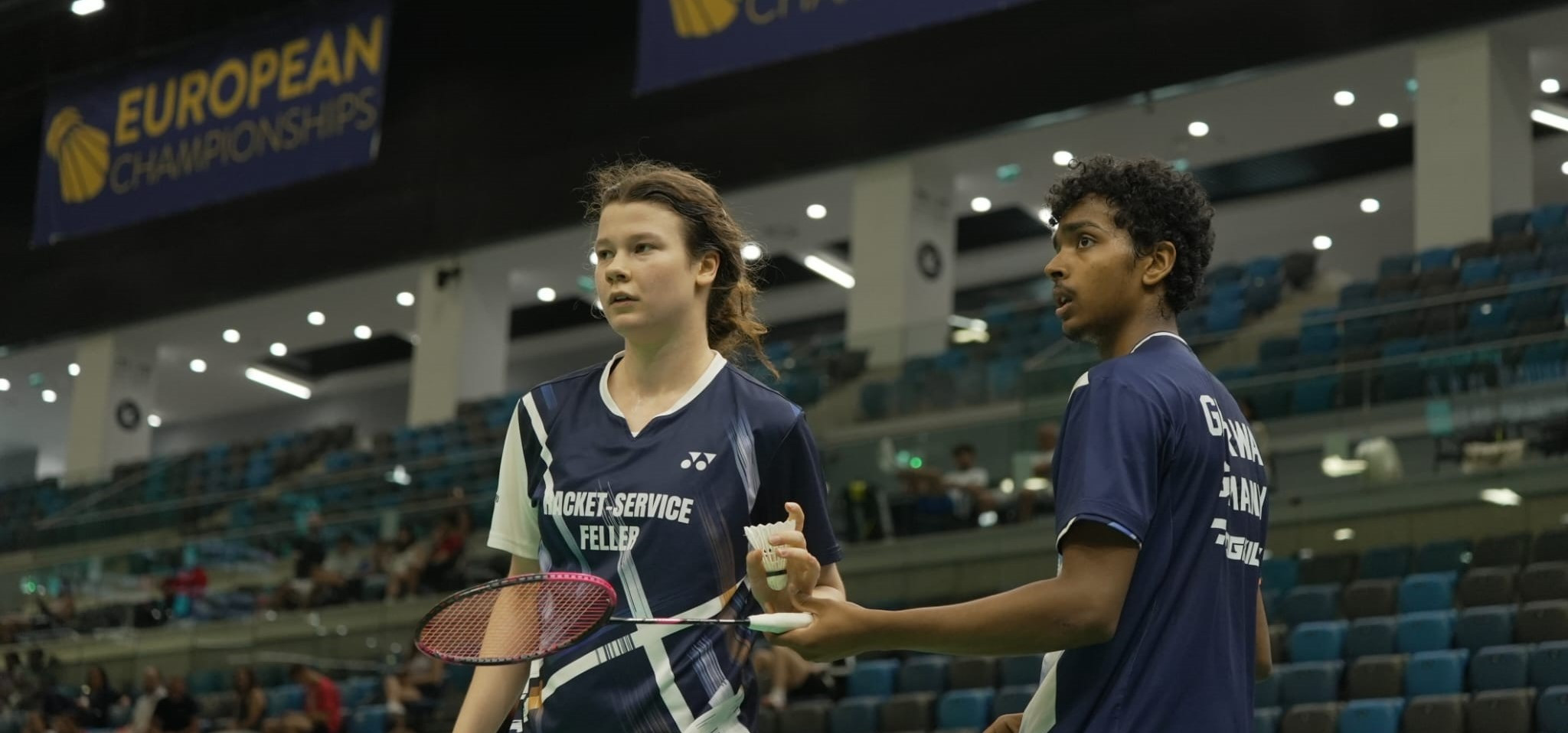 Zwei junge Badmintonspieler im Trikot von Racket-Service Feller auf einem Indoor-Badmintonfeld
