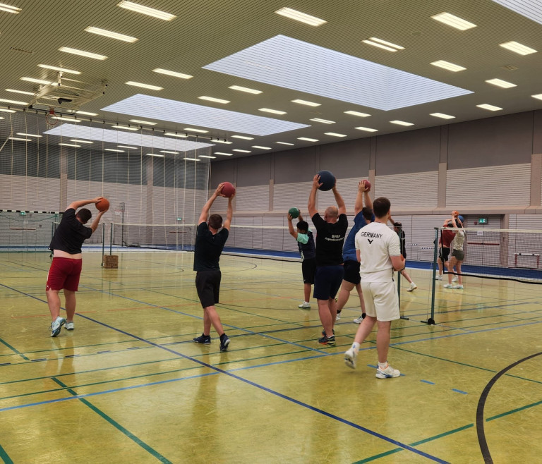 Teilnehmer beim Hobby-Breitensportcamp machen Aufwärmübungen mit Medizinbällen in einer Sporthalle