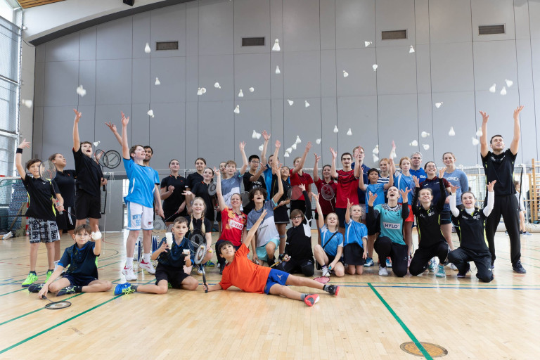 Gruppenfoto beim HYLO Open Training mit den besten Nachwuchsspielern in einer Sporthalle, alle werfen Federbälle in die Luft