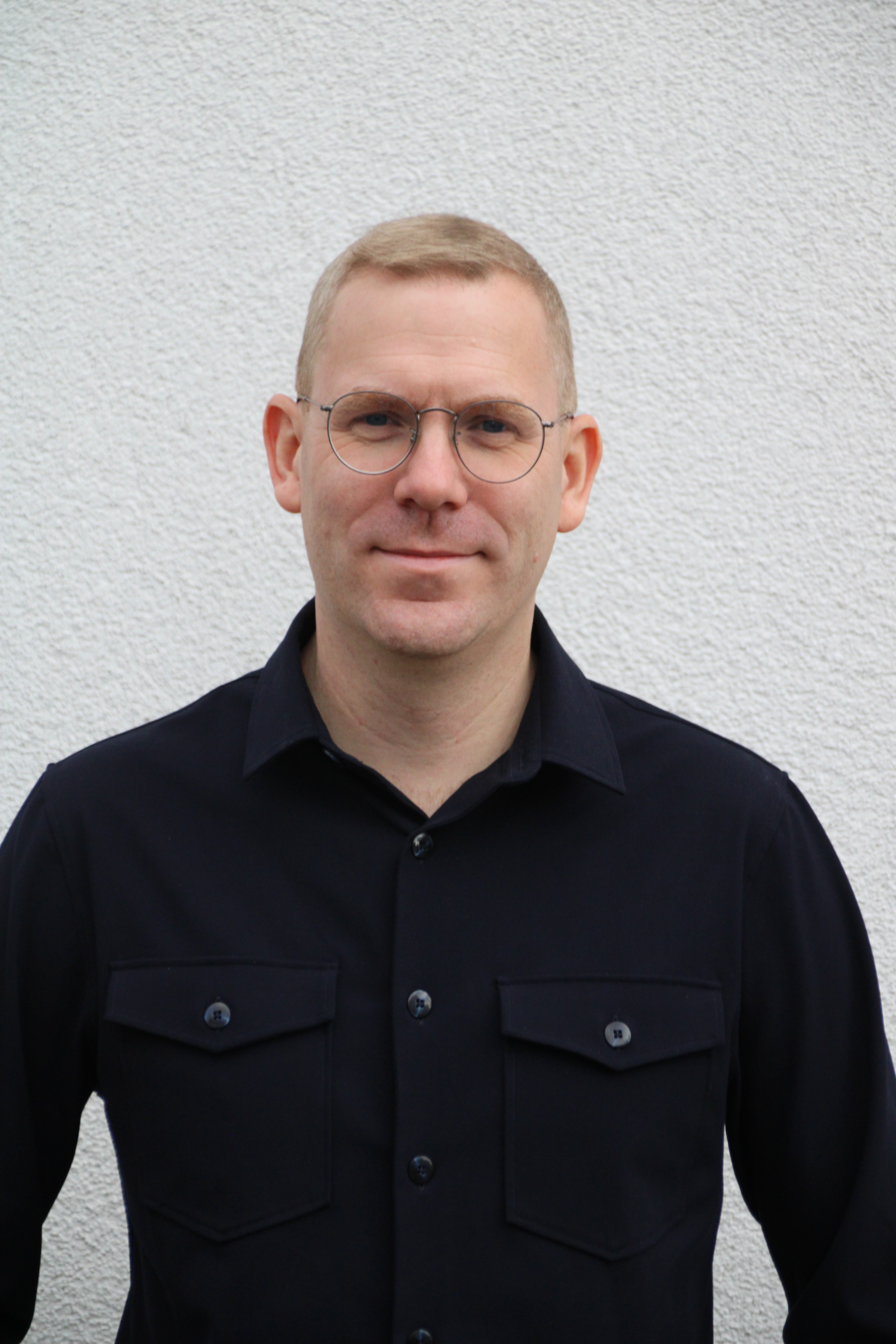 Mann mit dunklem Hemd vor weißer Wand