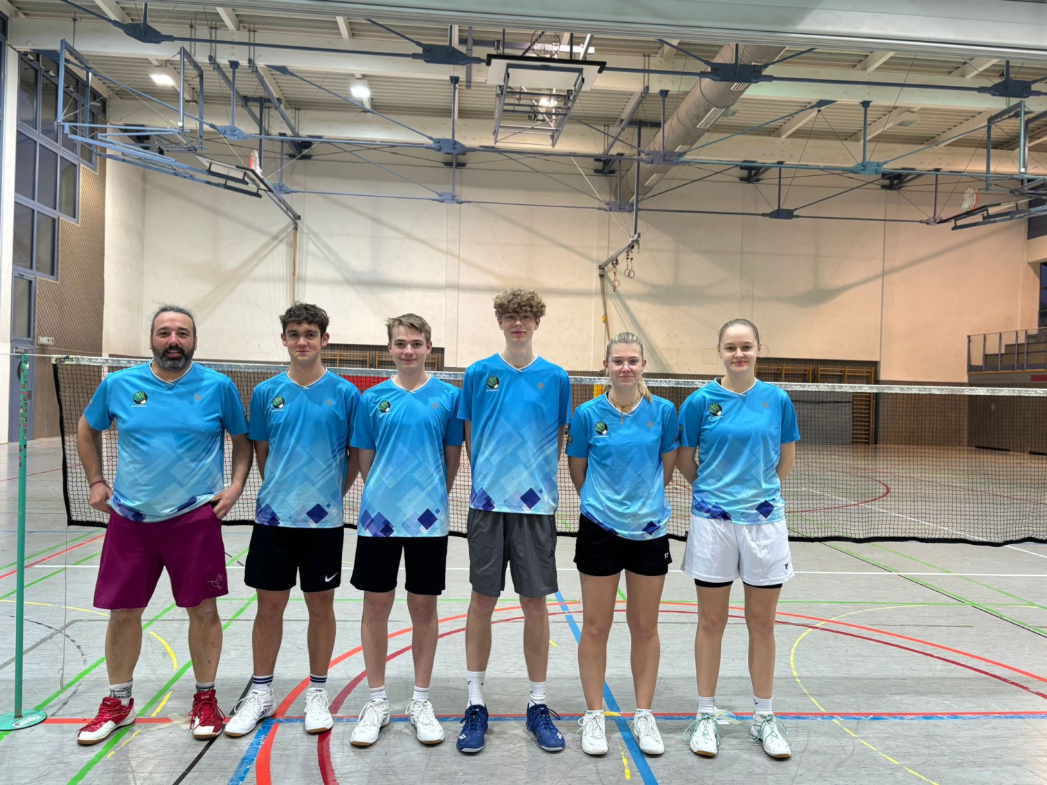 Badminton Mannschaft in blauen Trikots steht in Sporthalle vor einem Netz