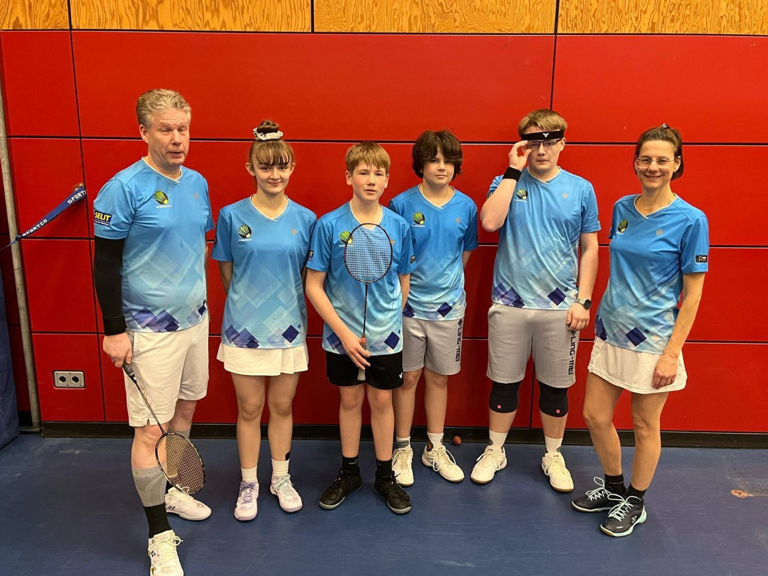Badminton Mannschaft in blauen Trikots vor roter Hallenwand