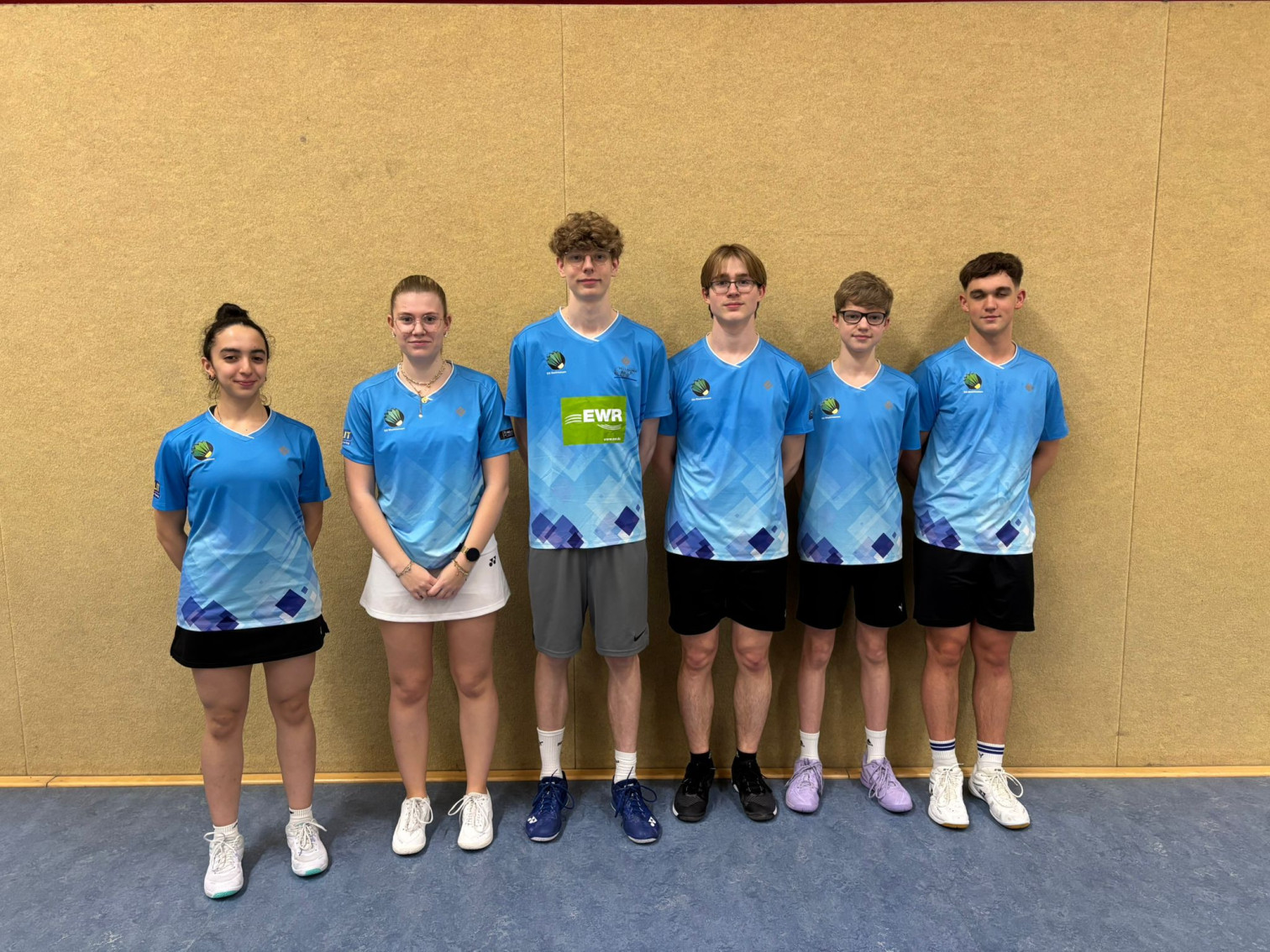 Badminton Mannschaft in blauen Trikots vor einer Hallenwand