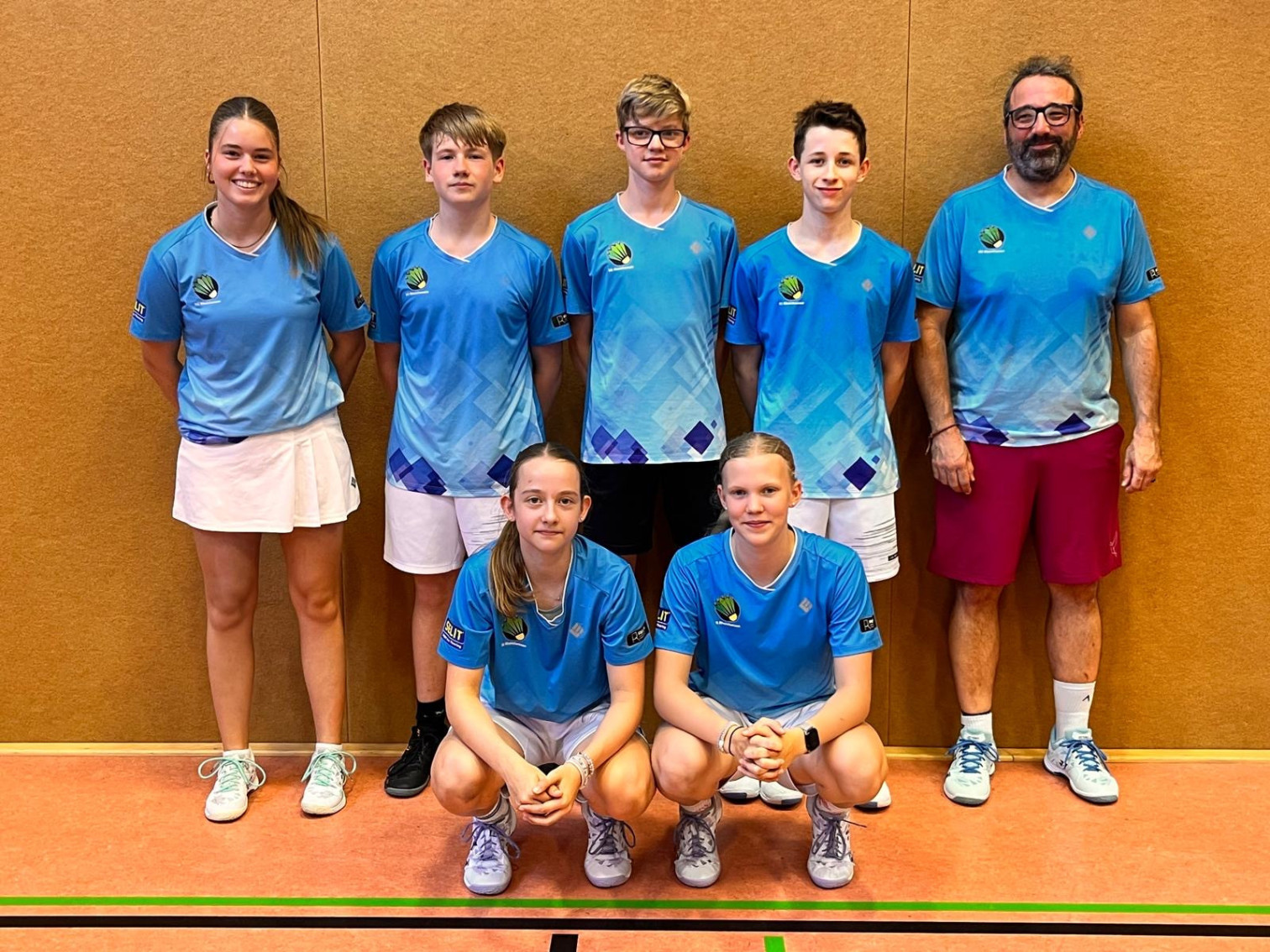 Gruppenfoto eines Badminton-Teams in blauen Trikots in einer Sporthalle