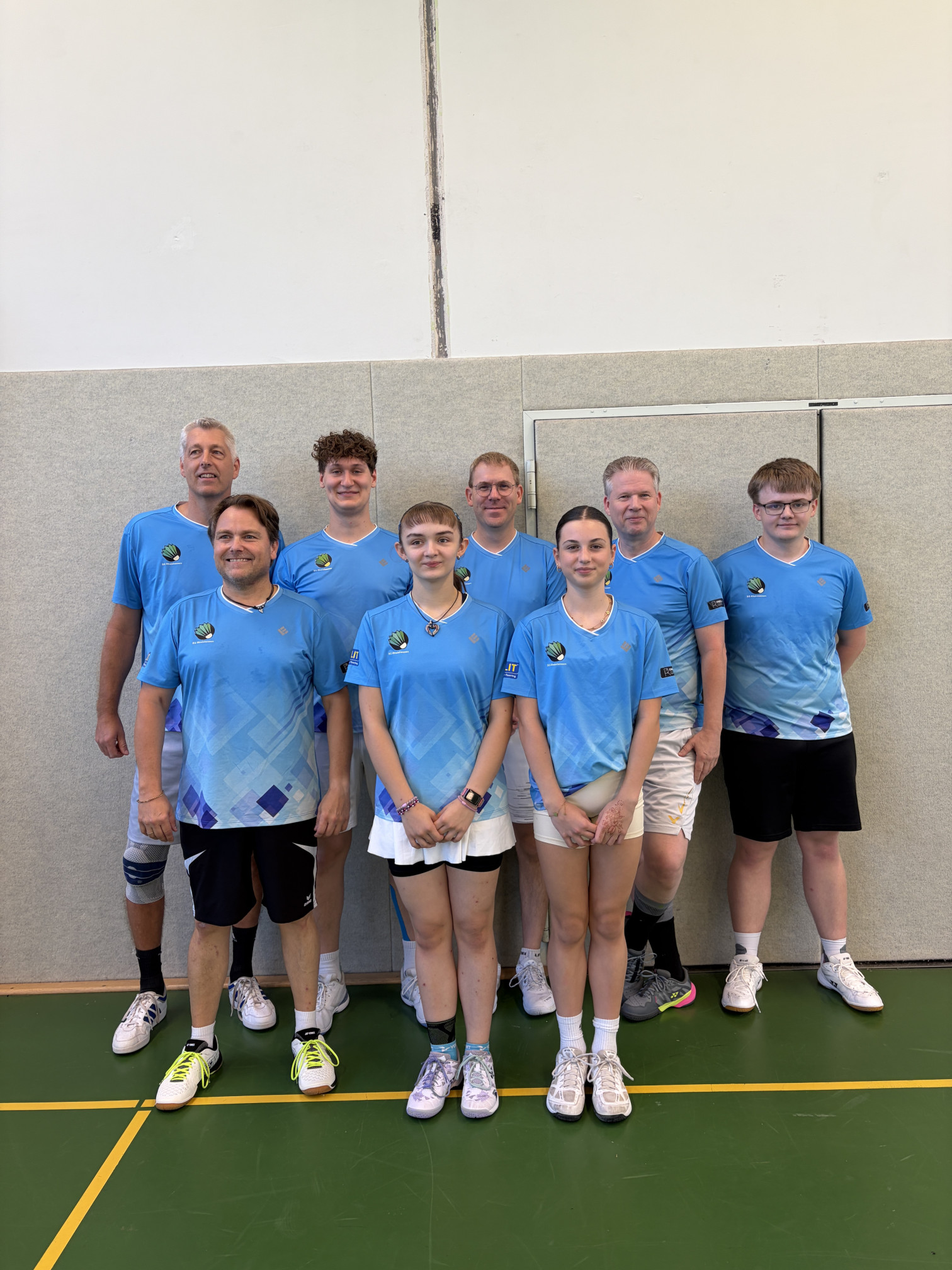 Gruppenfoto eines Badminton-Teams in blauen Trikots in einer Sporthalle
