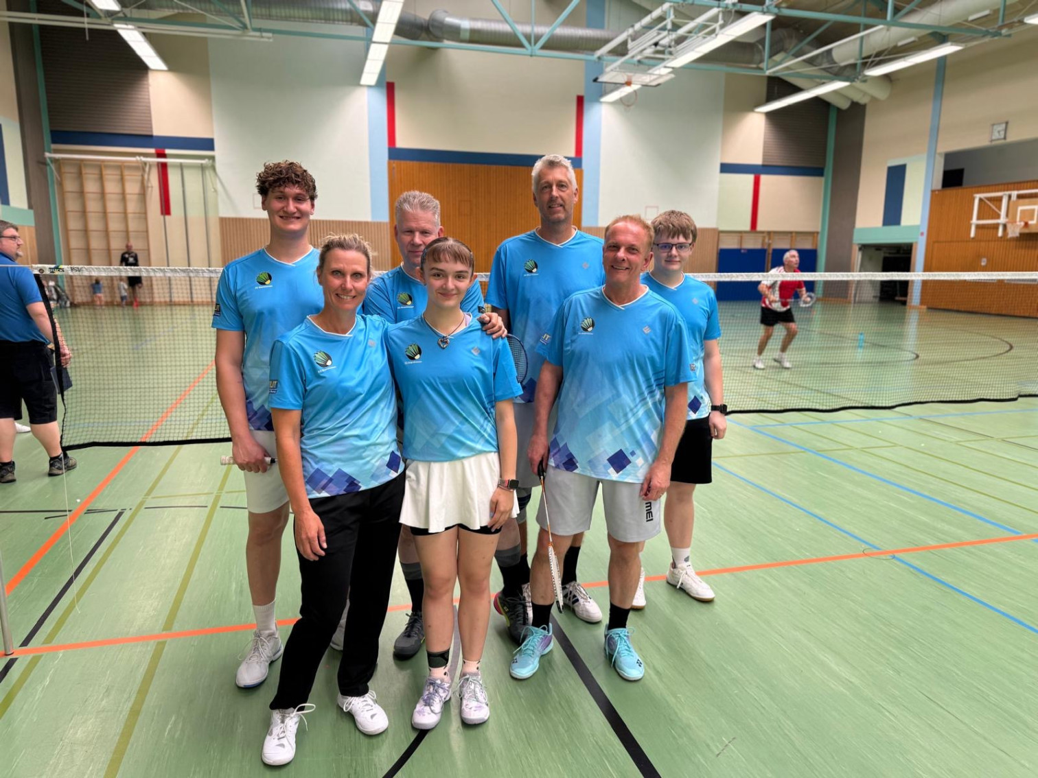 Badminton Mannschaft in blauen Trikots in einer Sporthalle vor dem Netz