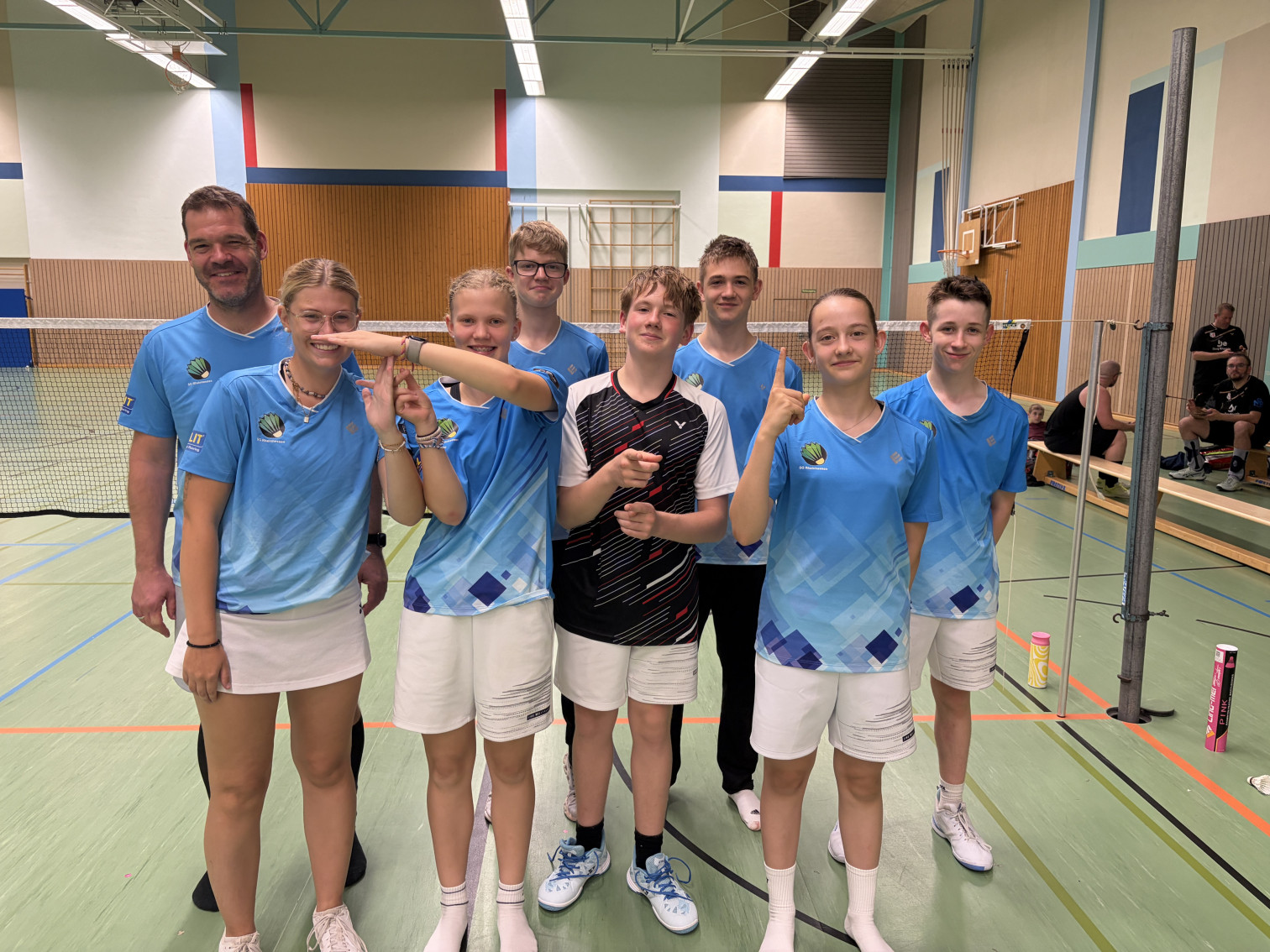 Jugendliche Badmintonmannschaft in blauen Trikots posiert in einer Sporthalle