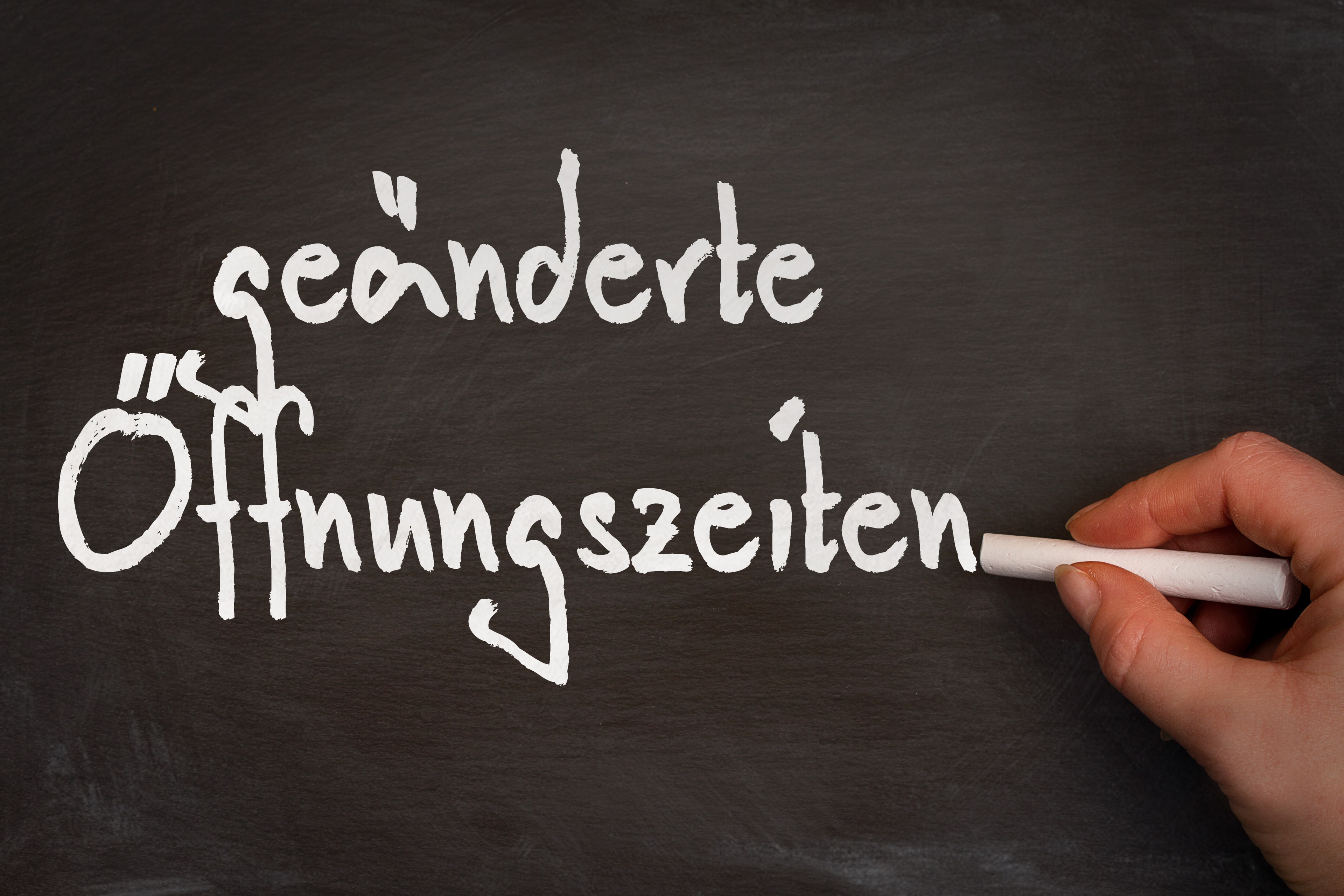 Hand schreibt geänderte Öffnungszeiten auf eine Tafel