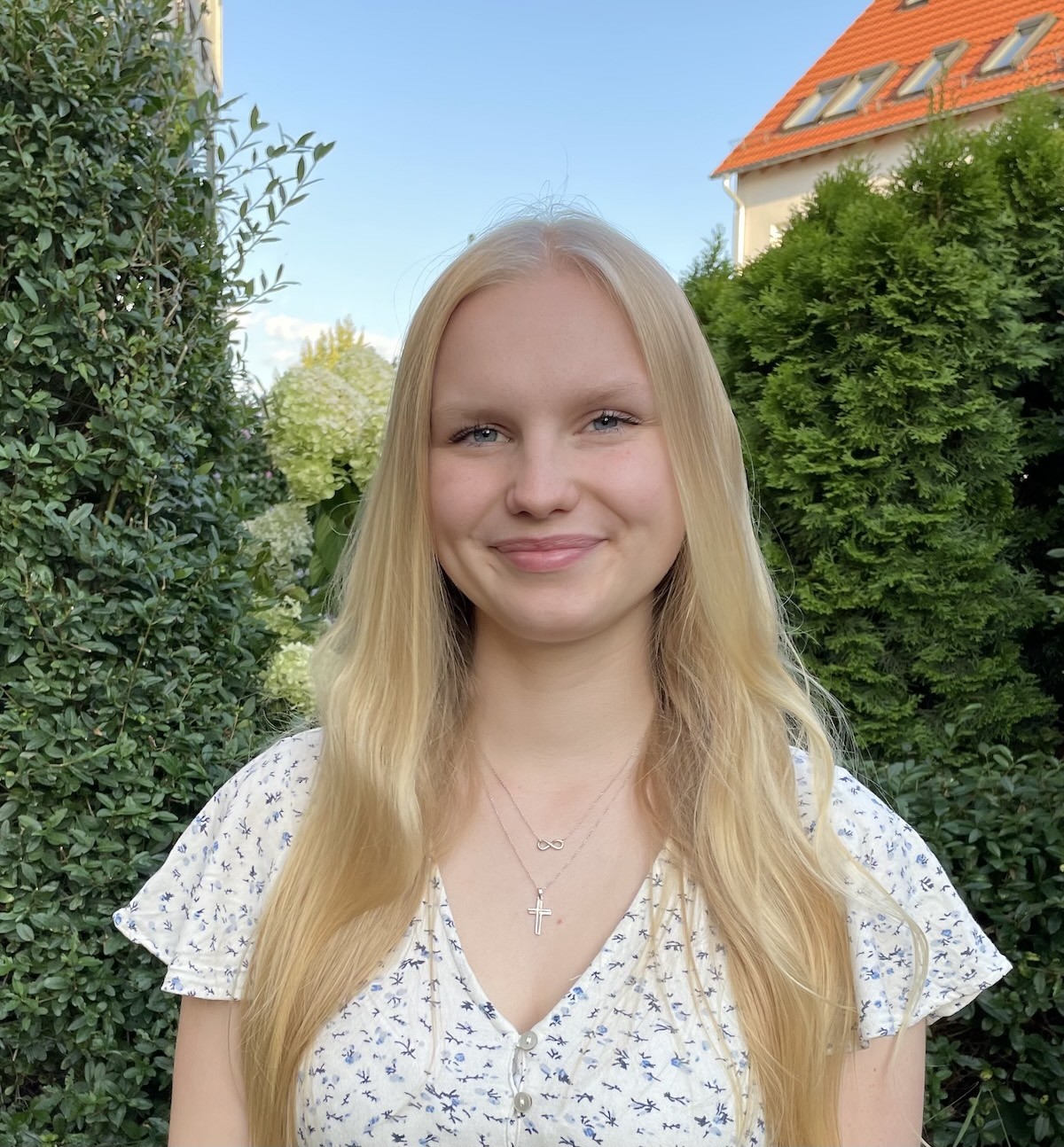 Junge Frau mit blonden Haaren lächelt im Garten