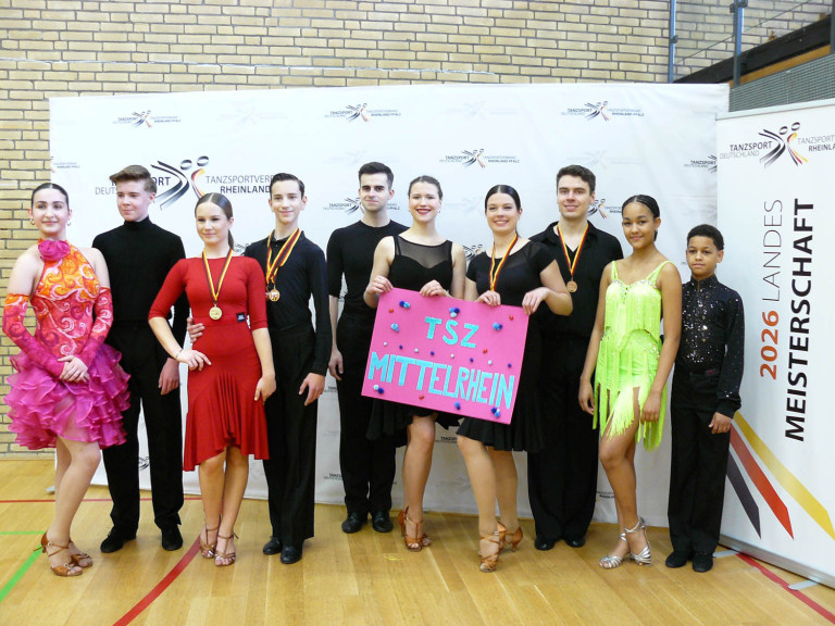Tanzsportgruppe des TSZ Mittelrhein bei einem Turnier mit Medaillen und Schild