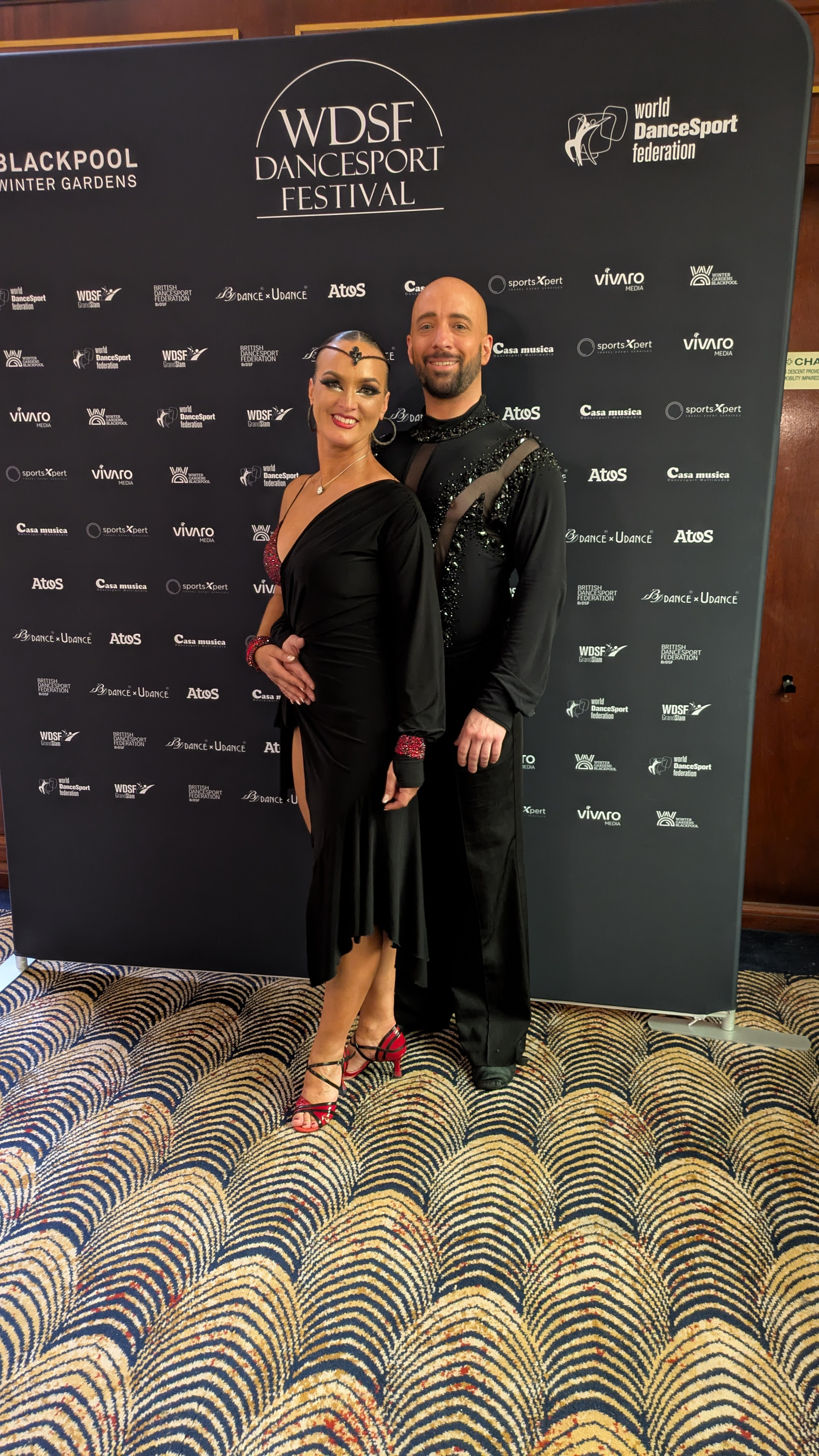 Tanzpaar in eleganter Turnierkleidung vor WDSF und British DanceSport Federation Fotowand
