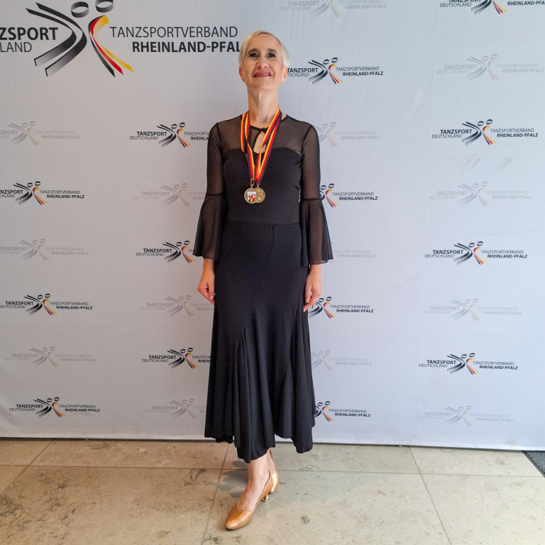 Landesmeisterschaft Tanzsportverband Rheinland-Pfalz – Siegerin mit Medaille Siegerin bei der Landesmeisterschaft des Tanzsportverbands Rheinland-Pfalz, elegant gekleidet mit Medaille vor offizieller Fotowand.